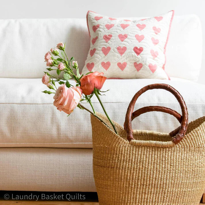 Woven basket with pink roses on a white couch with a heart-patterned pillow.